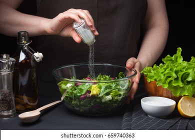 Woman chef in the kitchen preparing vegetable salad. Healthy Eating. Diet Concept. A Healthy Way Of Life. To Cook At Home. For Cooking. The girl sprinkles salt in a salad on a dark background - Shutterstock ID 659740363