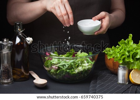 Woman chef in the kitchen preparing vegetable salad. Healthy Eating. Diet Concept. A Healthy Way Of Life. To Cook At Home. For Cooking. The girl sprinkles sea salt in a salad on a dark background