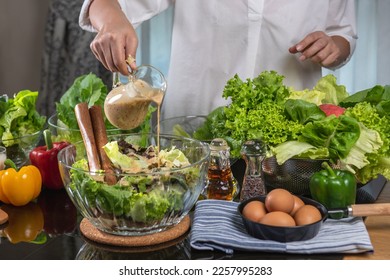 woman chef mix fresh baby cos salad and pour salad dressing in glass blow. Organic Vegetables mix all green salad In glass bowl. Breakfast fresh salad and clean vegetable. - Shutterstock ID 2257995283