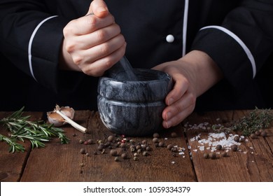 Woman Chef Pounding Spices And Herbs In Mortar For Food Cooking On A Black Background