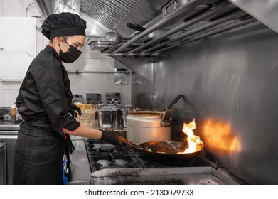 Woman Chef in protective face mask prepare food in the kitchen of a restaurant or hotel during new normal. Coronavirus prevention concept. High quality photo - Powered by Shutterstock