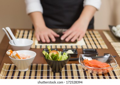 Woman chef ready to prepare japanese sushi rolls, with principal ingredients in the foreground