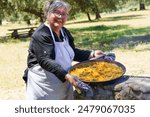 woman chef with white apron showing her typical Spanish paella cooked on the fire in the countryside