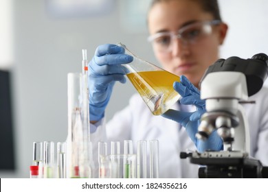 Mulher química segura frasco com líquido amarelo nas mãos no laboratório químico. Controle de qualidade do conceito de produtos petroquímicos.