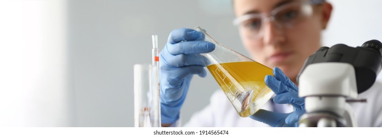 Woman Chemist Holds Flask With Yellow Liquid In Her Hands In Chemical Laboratory. Quality Control Of Petrochemical Products Concept.