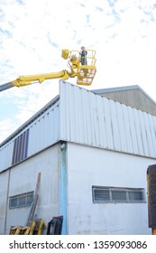 Woman In Cherry Picker Basket Above Industrial Building