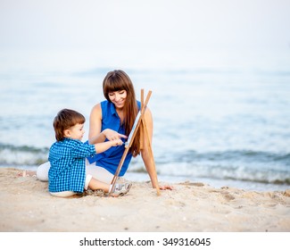 Woman And Child In Blue And White Dress Sit On The Beach And Draw On The Easel