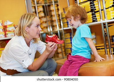 Woman With Child Choosing And Trying On New Boots In Shopping Supermarket