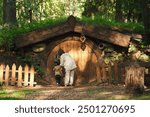 Woman and child entering a hobbit house with a round wooden door in a forest setting. Outdoor photography. Fairy tale and fantasy concept.