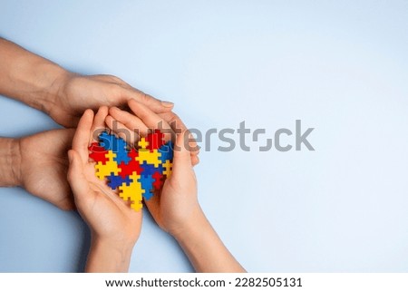 Woman and child hands holding together colorful puzzle heart on light blue background. World autism awareness day, Autism spectrum disorder concept