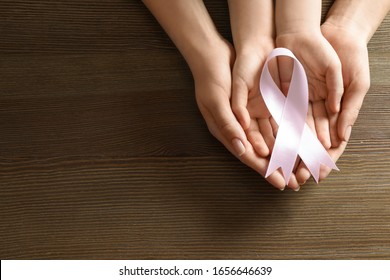 Woman and child holding pink ribbon on wooden background, top view with space for text. Breast cancer awareness - Powered by Shutterstock