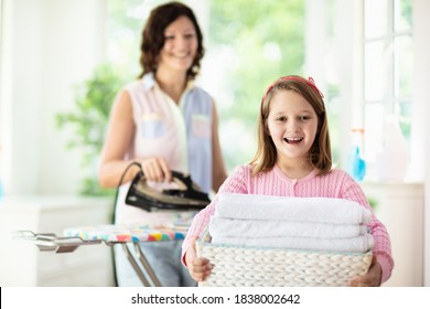 Woman And Child Ironing Clothes. Mother And Daughter Folding Clothes At Iron Board. Mom And Kid Cleaning House. Home Chores. 