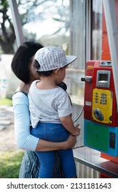 Woman And Child Mother And Kid Boy Baby Using Old Style Public Pay Phone In Telephone Booth