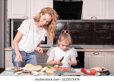 A Woman And A Child Are Preparing Sandwiches At Home Together. Mom And Daughter Together In The Kitchen. Copy Space.