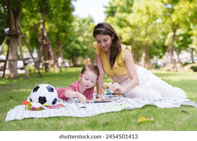 Woman and child sit on picnic blanket in park, coloring with art supplies, surrounded by greenery and a soccer ball. relaxing day for mother and son over the weekend. - Powered by Shutterstock