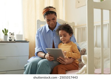 Woman and child sitting together on bed, using tablet in cozy bedroom setting, spending quality time and sharing learning experience - Powered by Shutterstock