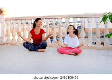 A woman and a child synchronously do warm-up exercises, laugh, practice yoga on the balcony against the backdrop of the city - Powered by Shutterstock