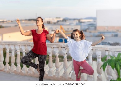 A woman and a child synchronously do warm-up exercises, laugh, practice yoga on the balcony against the backdrop of the city - Powered by Shutterstock