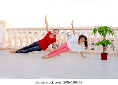 A woman and a child synchronously do warm-up exercises, laugh, practice yoga on the balcony against the backdrop of the city - Powered by Shutterstock