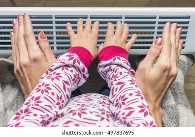 Woman and child warm up hands over electric heater.