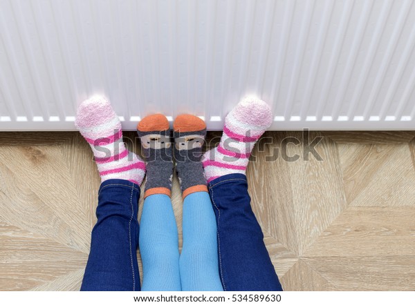 Woman and child wearing\
colorful pair of striped woolly socks warming cold feet in front of\
heater