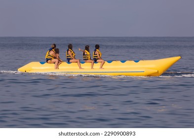 A woman with children rides on a yellow banana boat - Powered by Shutterstock