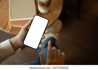 A woman is chilling in a cafe coffee shop and using her smartphone at a table while enjoying her coffee. A white-screen smartphone mockup for display your graphic ads. close-up image - Powered by Shutterstock