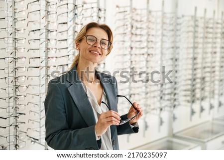 Woman chooses between two spectacle frames in an optician's shop and looks at the camera