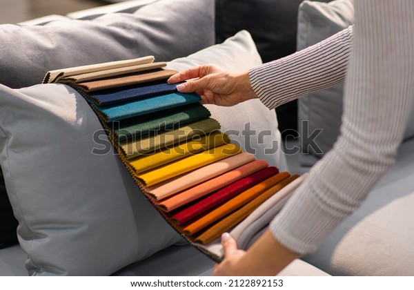 The woman chooses the fabric\
on the sofa. A young women looks at tissue samples. Selects the\
color of the sofa. Textile industry background. Tissue\
catalog