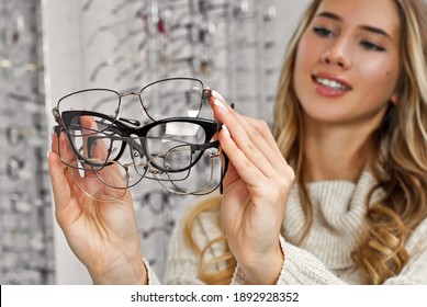 Woman chooses glasses in the store. Blonde in a beige sweater buys glasses. Girl on a background of shop windows with different models of glasses.