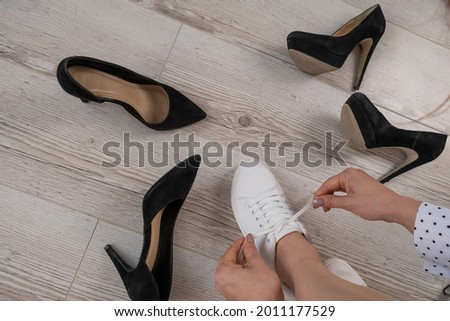 A woman chooses sports shoes instead of high-heeled shoes. Sneakers or shoes