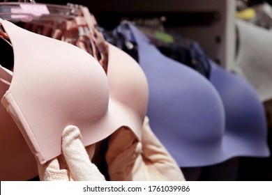 Woman chooses wireless bra hanging on rack in lingerie store, female hands in protective gloves. Concept of shopping, customer during sale, different sizes of sexy underwear