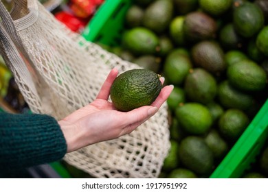 Woman choosing avocados in the supermarket. Close up of hand holding avocado in farm market. - Powered by Shutterstock