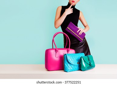 Woman choosing the bag from many colorful bags.Isolated on light blue background. Shopping addiction. 