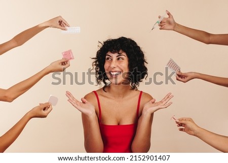 Woman choosing between hormonal and non-hormonal contraceptives. Happy young woman smiling while surrounded by different forms of contraception. Woman taking control of her reproductive health. [[stock_photo]] © 
