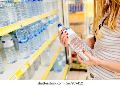 Woman Choosing Bottled Mineral Water In Supermarket Store