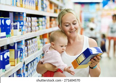 Woman Choosing Children Food With Little Baby Child Girl On Hands During Supermarket Shopping