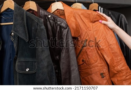 Woman choosing clothing in a second hand store. Various vintage suede leather and jeans jackets hang on clothing rack. Thrifting and sustainability in clothing concept