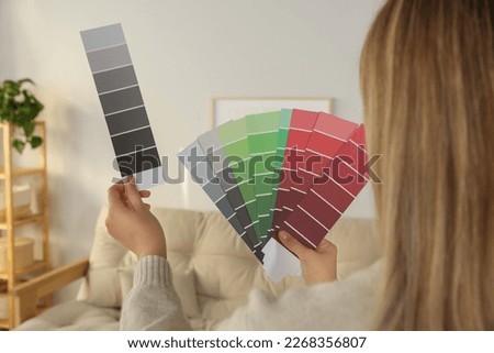 Woman choosing color for wall in room, focus on hands with paint chips. Interior design