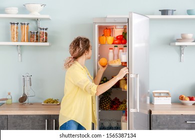 Woman Choosing Food In Modern Fridge At Home