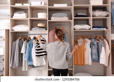 Woman choosing outfit from large wardrobe closet with stylish clothes and home stuff - Shutterstock ID 1293384706
