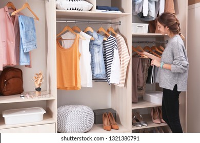 Woman choosing outfit from large wardrobe closet with stylish clothes, shoes and home stuff