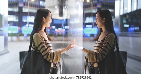 Woman Choosing Product Inside Shop Window In The City At Night With Window Reflection 