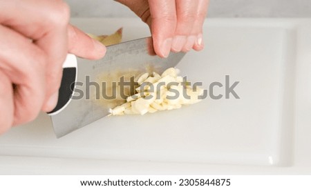 A woman chops fresh garlic using a kitchen knife, close-up view