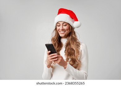 Woman christmas Santa Hat white sweater white studio background with smartphone in hand Beautiful caucasian female curly hair portrait. Happy person positive emotion Holiday concept Teeth smiling  - Powered by Shutterstock