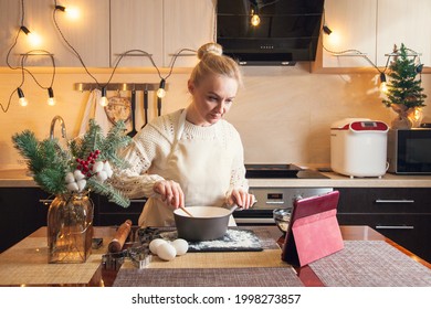 Woman In Christmas Sweater Following Recipe On Digital Tablet And Cooking Dough On Her Kitchen.