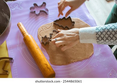 Woman in Christmas sweater making gingerbread cookies in different forms at domestic kitchen. Rolling pin and cookies form at the table with woman chef. Preparing homemade cookies. Christmas time. - Powered by Shutterstock