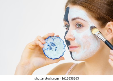 Woman with clay carbo black mask on half face applying white mud to clean skin. Girl taking care of oily complexion. Beauty procedures. Skincare.