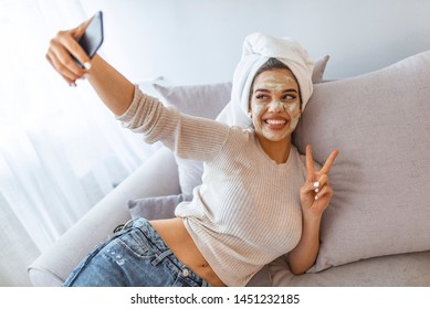 Woman With Clay Mask Taking Selfie With Mobile Phone At Home Enjoying Relaxation And Beauty Treatment.Woman With Facial Clay Mask Making Selfie On Her Smartphone