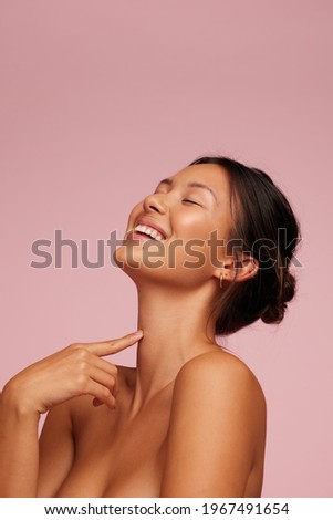 Woman with clean and clear skin smiling. Female model with eyes closed against pink background.